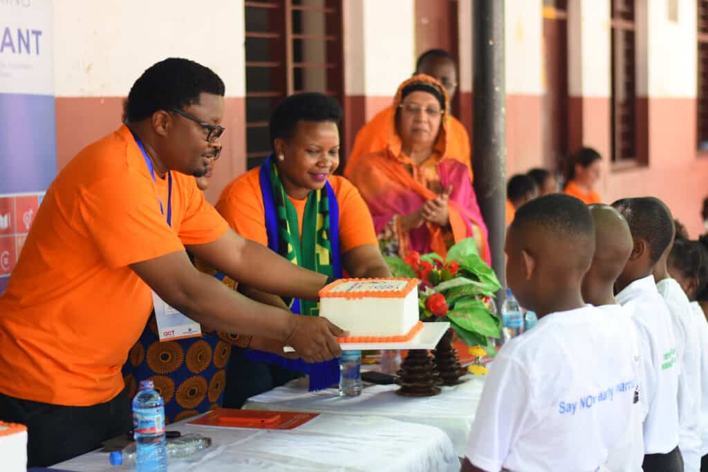 A male and female volunteer dressed in orange hand out cake at an event to promote gender equality in Kenya