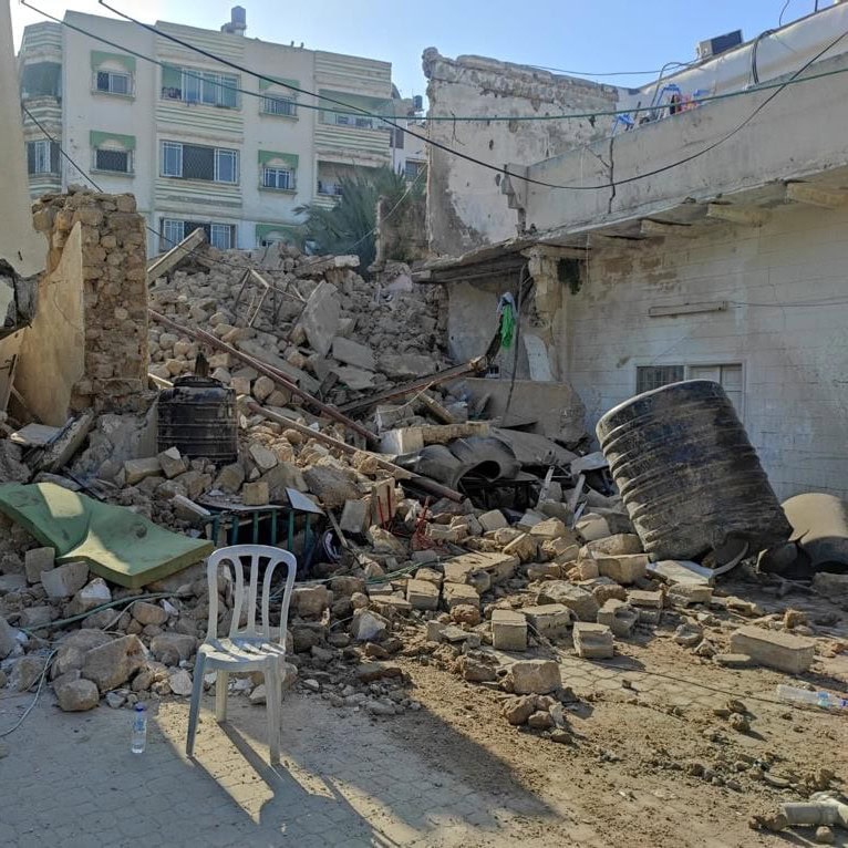 Collapsed residential building with rubble and a plastic chair in the foreground, 2024.